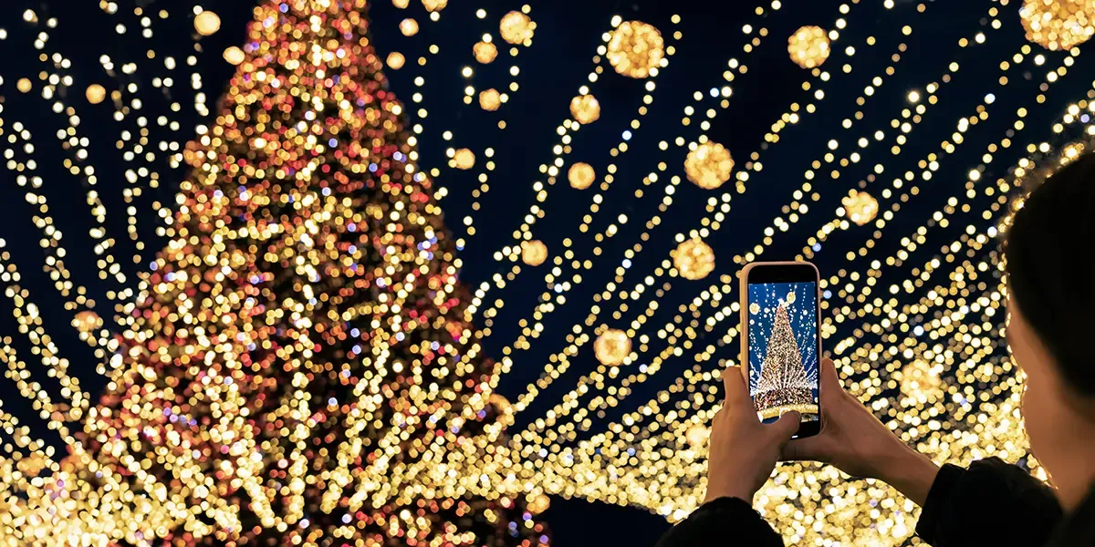 A woman take a picture of a christmas tree and light display with her phone